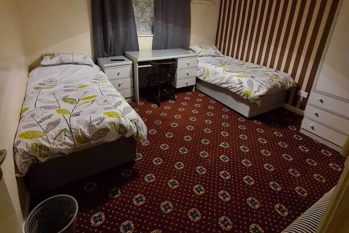 A compact hotel room with two single beds, a desk, a chair, and a radiator.
