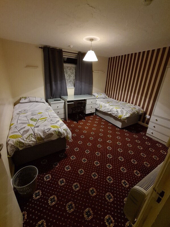 Una habitación de hotel compacta con dos camas individuales, un escritorio, una silla y un radiador.