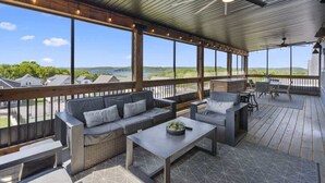 A covered outdoor patio with a sofa, chairs, and a table, overlooking a lake and greenery. - Westview - Indoor pool & lake views (Branson)