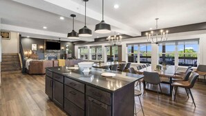 A spacious kitchen with a large island, modern pendant lighting, and a view of the outdoors through large windows. - Westview - Indoor pool & lake views (Branson)