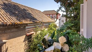 Ein Innenhof mit Ziegeldach, einer weißen Wand mit Fenster und üppiger Bepflanzung, darunter große weiße Blüten und Farne.