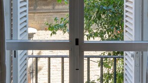 Blick durch ein Fenster mit weißen Fensterläden auf ein Ziegeldach und eine Backsteinmauer.