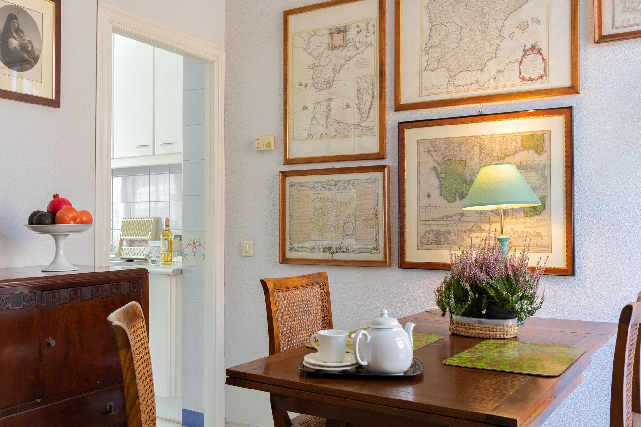 A dining area with a wooden table, chairs, a white teapot, and a lamp.
