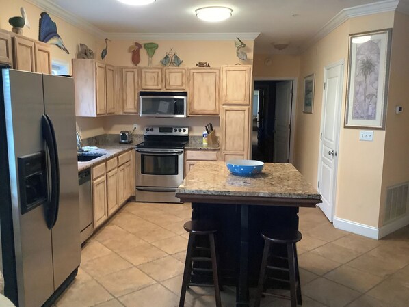 A kitchen with wooden cabinets, a stainless steel refrigerator, a microwave, an oven, and a granite countertop with a blue bowl. - HARBORWALK Destin with boatdock (Destin)
