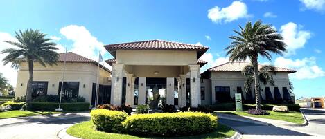 A two-story building with a central entrance, flanked by palm trees and well-maintained hedges.
