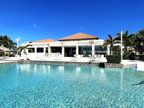 A poolside area with a clear blue pool, white lounge chairs, and a building with a tiled roof.