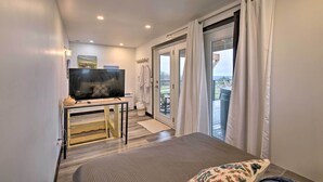 Habitación de hotel con una cama, un televisor sobre un mueble, una mesita y vistas al exterior a través de una puerta corredera.