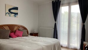 Une chambre à coucher avec un lit, un radiateur, une fenêtre avec des rideaux et un mur orné d’un tableau.