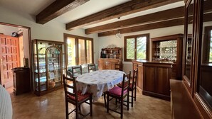 Un coin repas avec une table ronde, des chaises en bois, un buffet contenant de la verrerie, et une vue sur l’extérieur par une fenêtre.