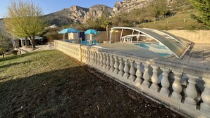 Un espace piscine agrémenté de chaises longues et de parasols, une balustrade en pierre et un paysage montagneux en toile de fond.