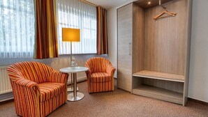 A hotel room with striped armchairs, a small round table, a lamp, a wardrobe, and a window with curtains. - Hotel Goldene Krone (Goslar)