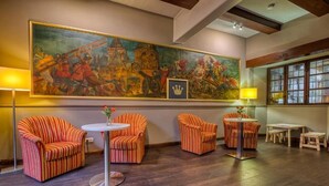 A lobby with striped armchairs, a round table, and a large historical painting. - Hotel Goldene Krone (Goslar)