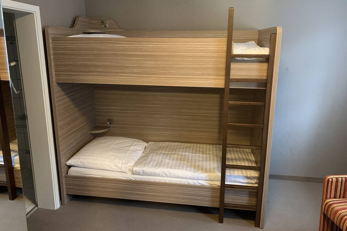 A bunk bed with a wooden frame and a ladder, a small shelf, and a bedside table.