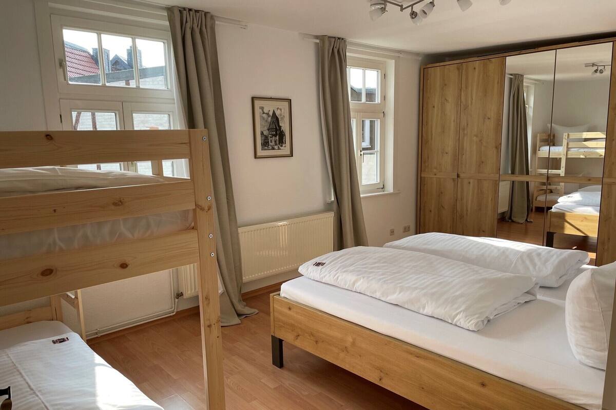 A room with a wooden bunk bed, a single bed, a wardrobe, and a window with curtains.