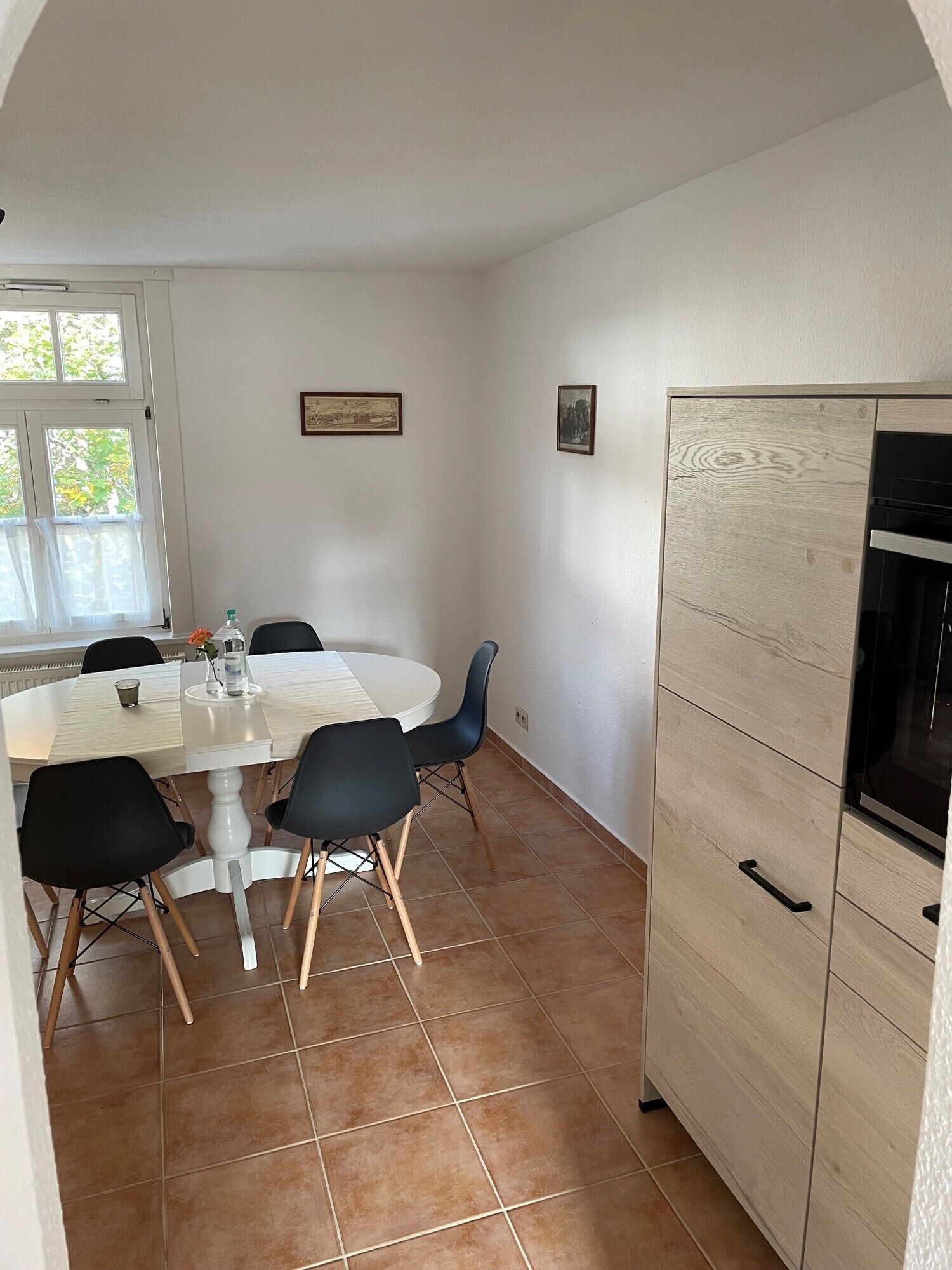 A dining area with a round table, black chairs, and a white cabinet with a black oven.
