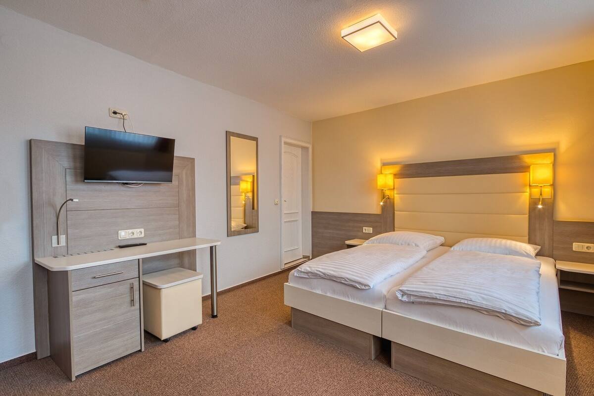 A hotel room with a bed, bedside tables, a TV, a desk, and a mirror.