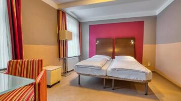 Habitación de hotel con cama, una silla, una mesita y ventana con cortinas.