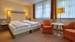 A hotel room with two beds, a round table with chairs, and a large window with curtains. - Hotel Goldene Krone (Goslar)