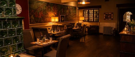 Un restaurante tenuemente iluminado con mesas y sillas de madera, un muro decorativo verde y un cuadro grande.