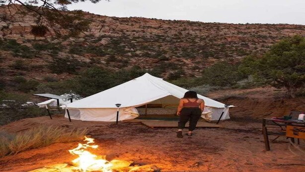 Un terrain de camping avec une tente, un foyer et une table sur laquelle se trouvent divers objets.