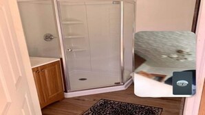 Une douche d’angle avec une porte en verre, un meuble en bois et un tapis à motifs.
