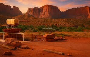 A desert landscape with a covered wagon on a dirt road, surrounded by large rocks and sparse vegetation.