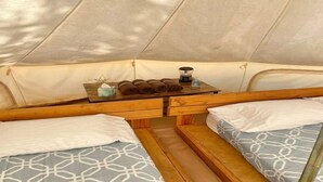 L’intérieur d’une tente avec deux lits, une table avec des serviettes et une petite table avec une lampe.