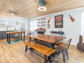 A spacious dining area with a wooden table and benches, a chandelier, and a violin on the wall.