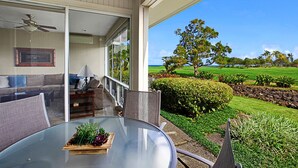 Una mesa con cubierta de vidrio, un centro de mesa floral, un sofá y un ventilador de techo en una habitación con vista a un campo de golf.