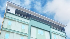 Un hotel de varios pisos con fachada verde, un cartel que dice 'Leaf Hotel' y plantas en macetas en la entrada.