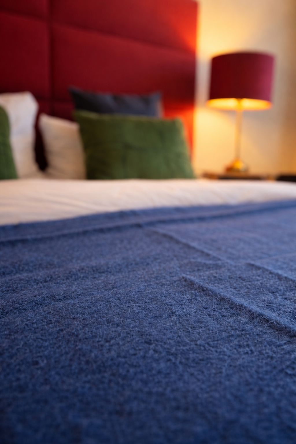 Un lit avec une couverture bleue, une tête de lit rouge et une lampe sur une table de chevet.