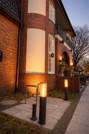 A brick building with a white facade, a balcony with a railing, and a sign that reads "The Lodge." - Sleephotels Suite Garde (Hamburg)
