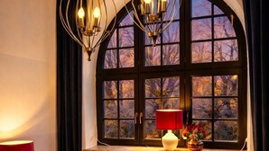 A hotel room with a large arched window, a red lamp, a red chair, and a bed with a blue blanket. - Sleephotels Suite Garde (Hamburg)