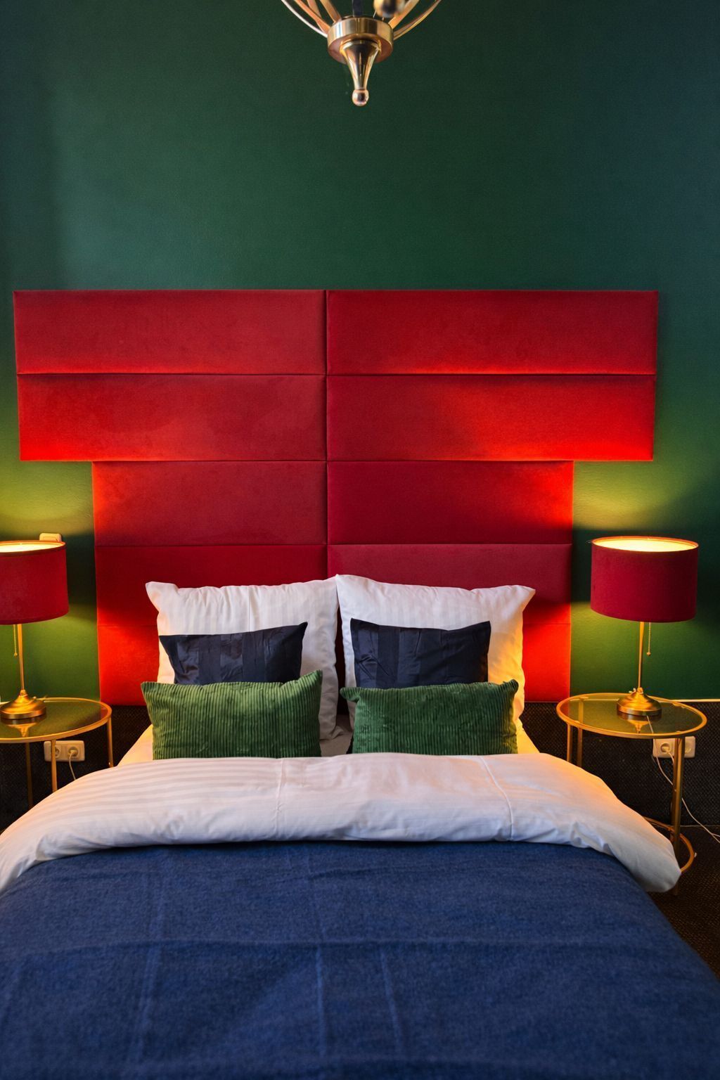 A bed with a red headboard, white and green pillows, and two bedside lamps.