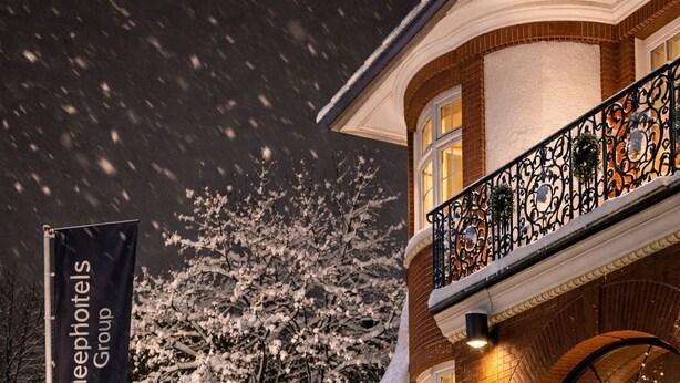A snow-covered building with a sign for Sleepyholts Group, a brick facade, and a balcony with decorative railings. - Sleephotels Suite Garde (Hamburg)