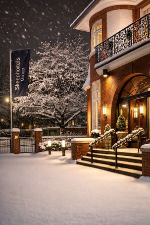 A snow-covered building with a sign for Sleepyholts Group, a brick facade, and a balcony with decorative railings. - Sleephotels Suite Garde (Hamburg)