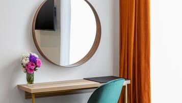 A desk with a laptop, a vase of flowers, and a round mirror on the wall.