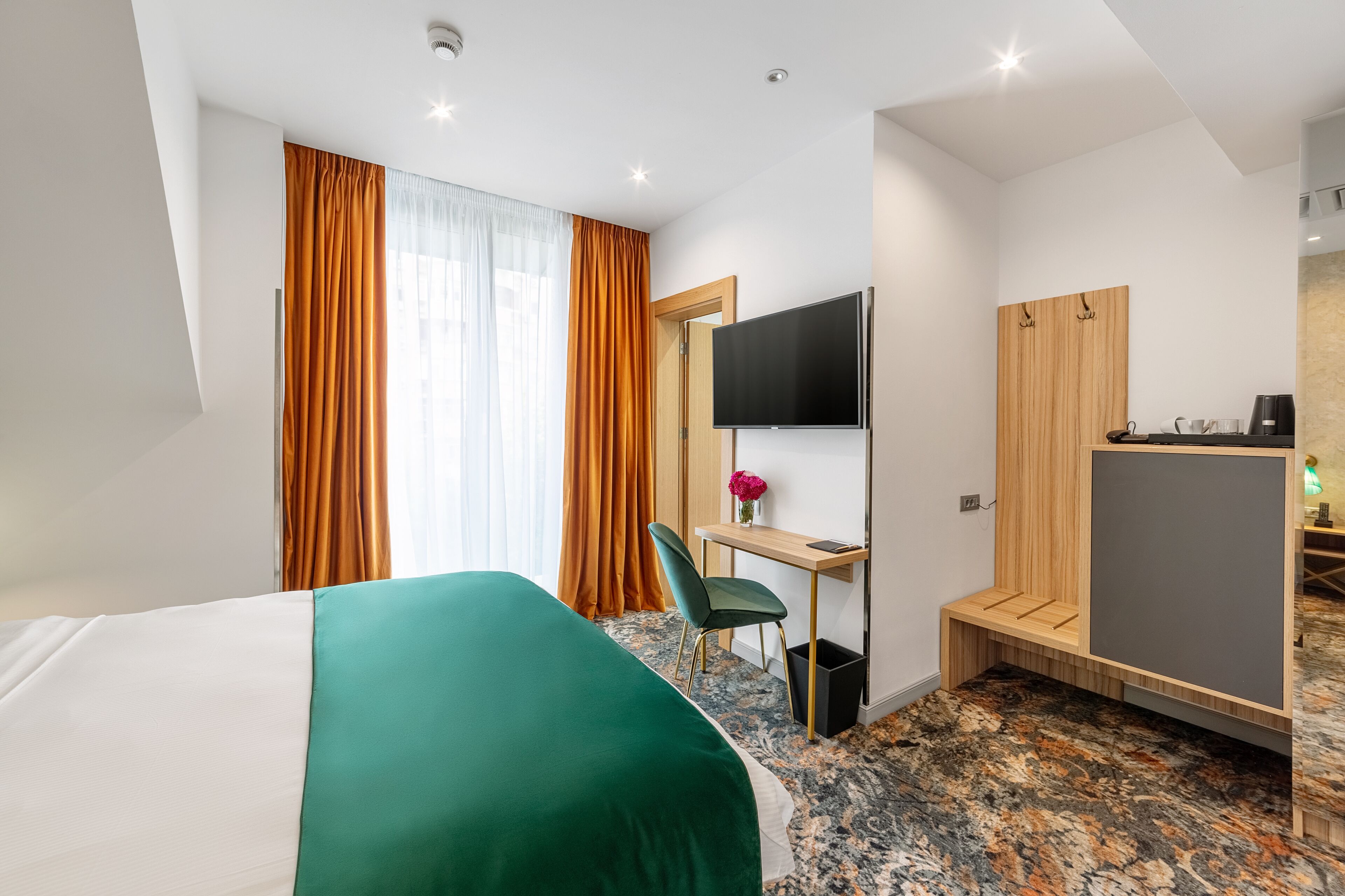 Une chambre d’hôtel équipée d’un lit, d’un bureau, d’une chaise, d’une télévision, d’une armoire et d’une petite kitchenette.