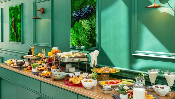 Un buffet de petit-déjeuner proposant divers plats et boissons, le tout présenté sur un comptoir en bois devant un mur vert.