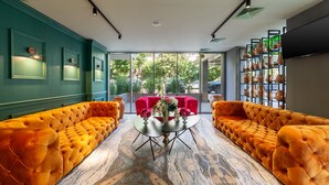 Un hall d’entrée moderne avec un sol en marbre, deux canapés orange à motifs capitonnés, une table ronde centrale ornée d’un vase de fleurs et, au fond, un canapé rouge.