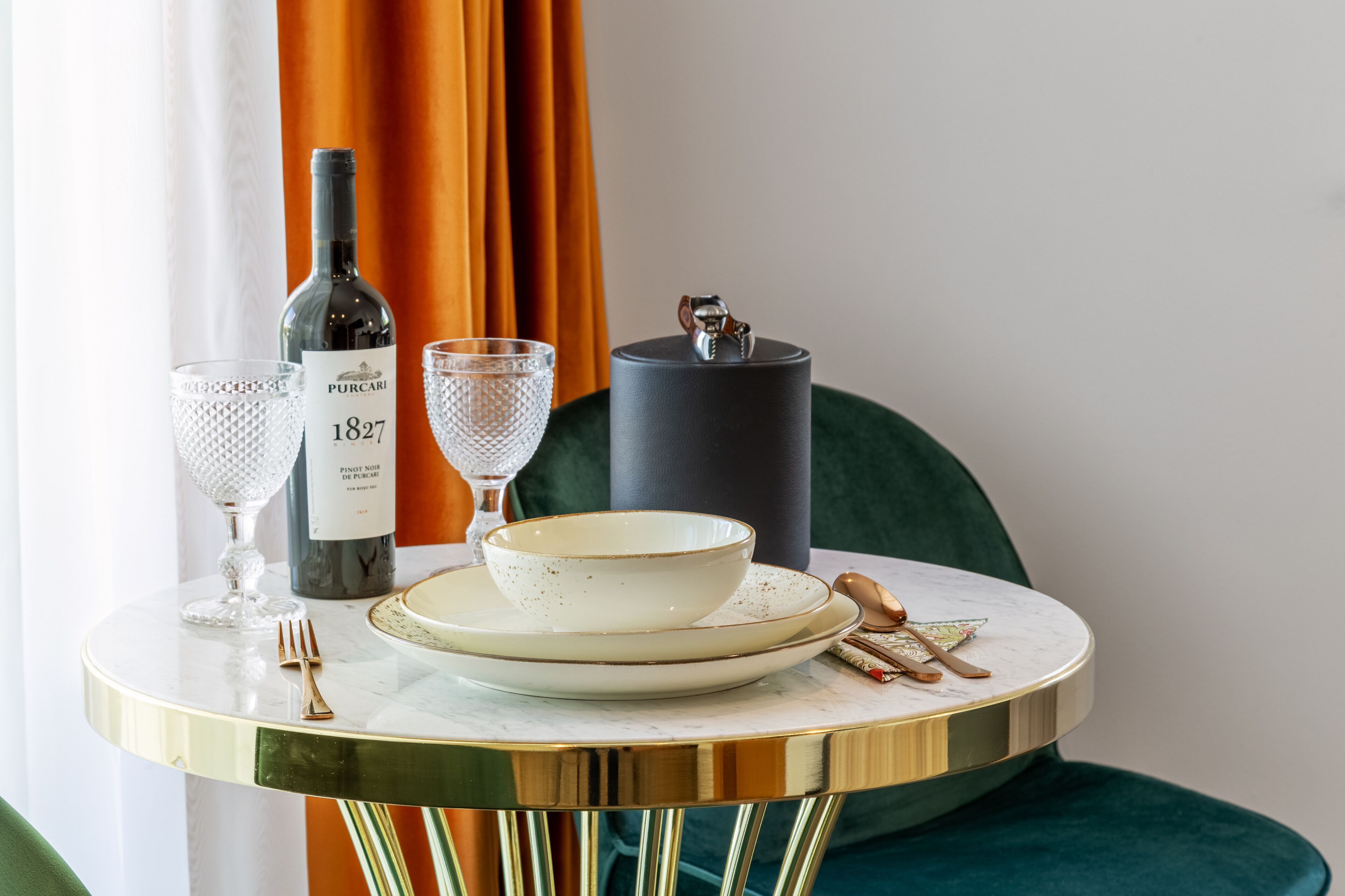 A table with a bottle of wine, two wine glasses, a bowl, and cutlery.