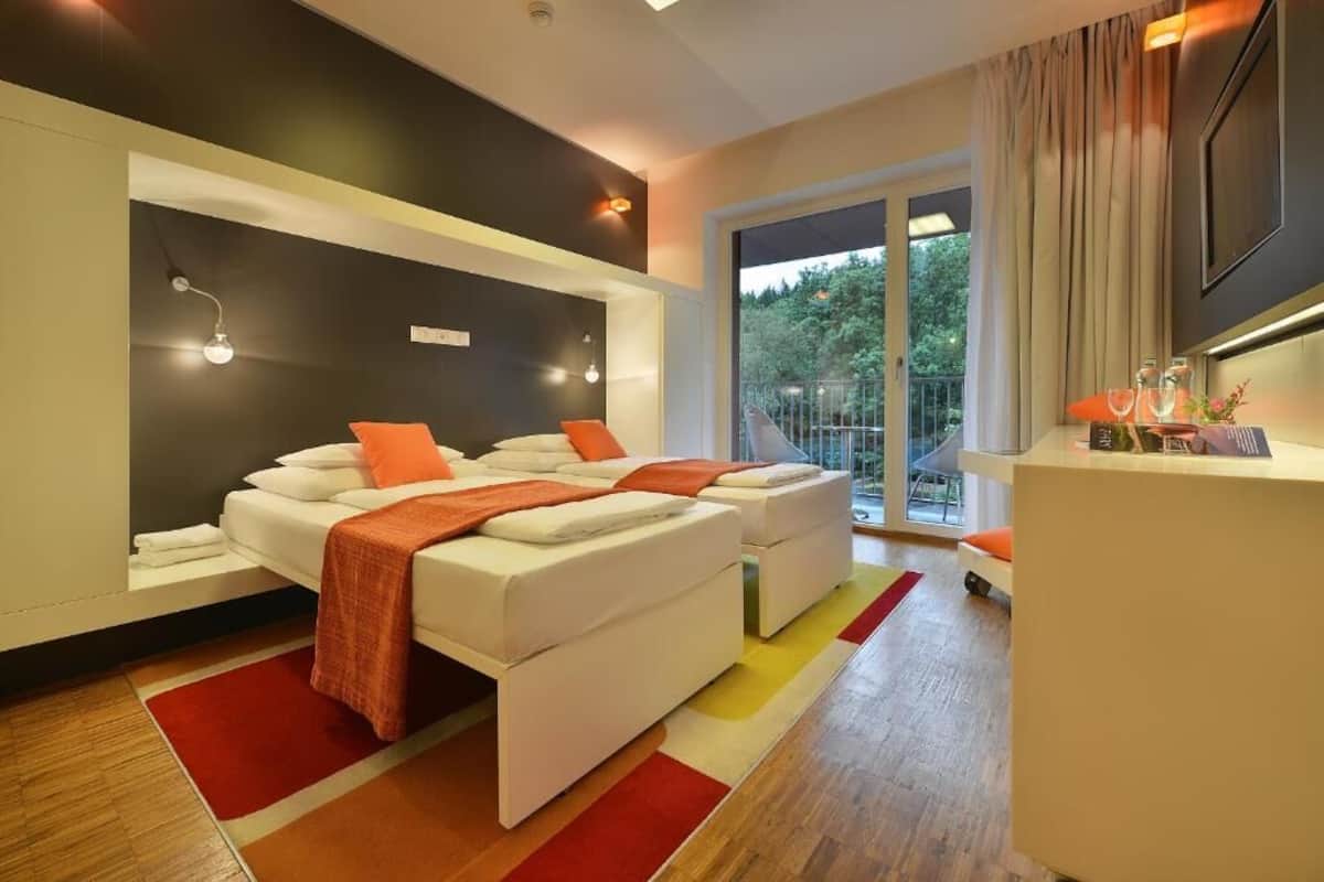 A modern bedroom with a large bed, a desk, and a view of the outdoors.