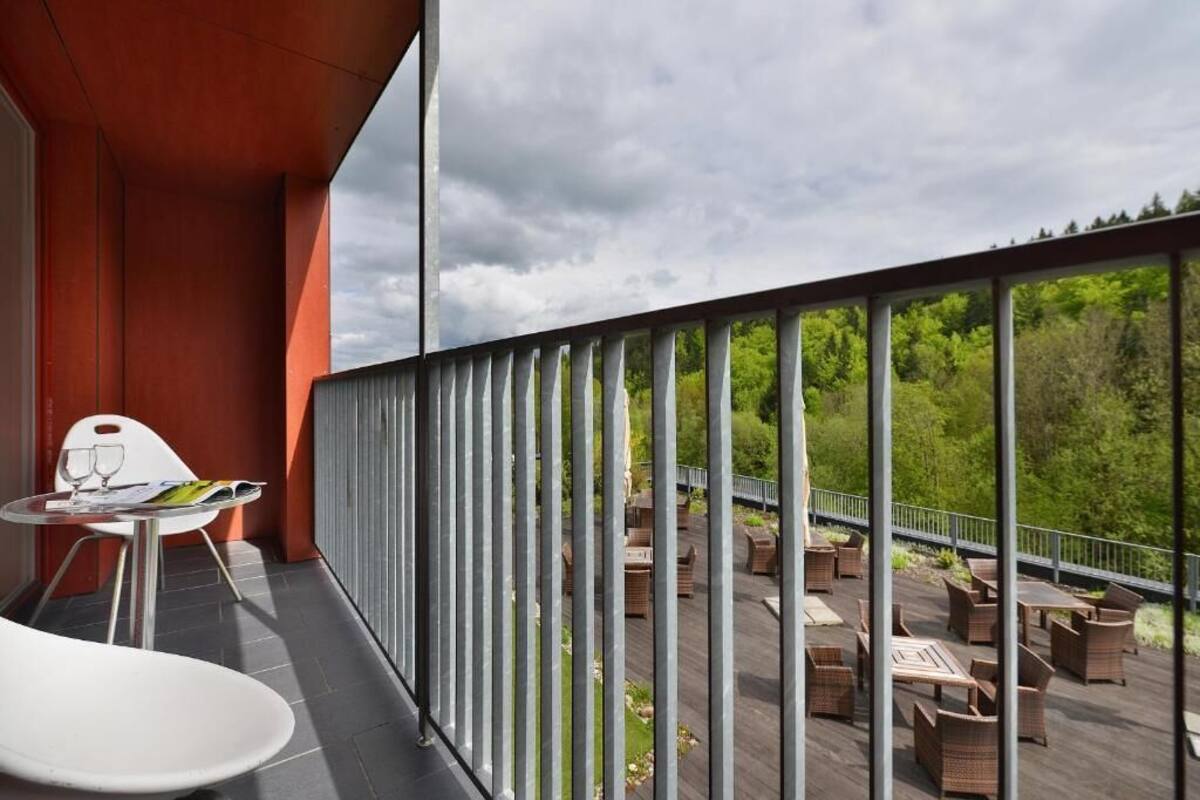 A balcony with a view of a forest, outdoor seating, and a table with a glass.