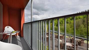 Een balkon met uitzicht op een bos, buitenzitplaatsen en een tafel met een glas.