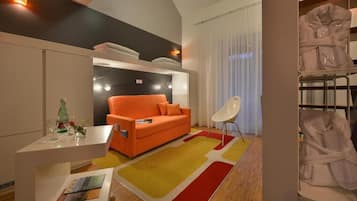 Et moderne hotelværelse med en sofa, et lille bord med en flaske og glas, en stol og et stort vindue med gardiner.