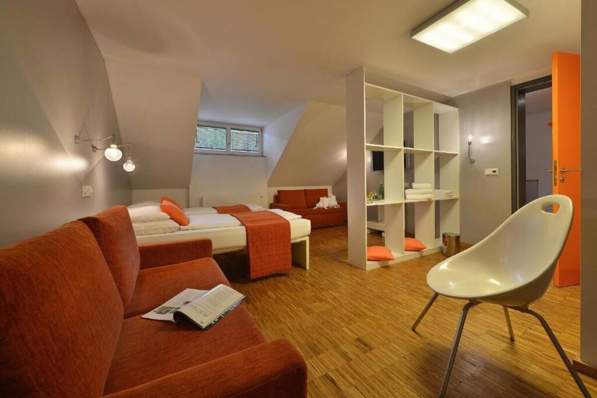 A modern, compact room with two beds, a sofa, and a white chair.