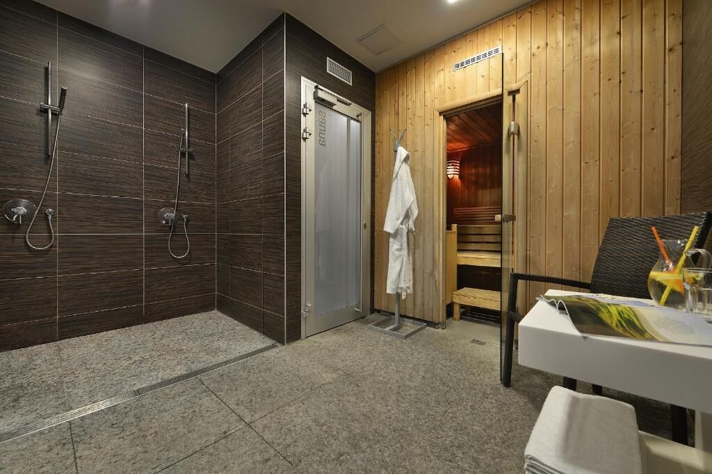 A modern bathroom with dark wood paneling, a shower area, a wooden door, and a table with a magazine and a glass of water.