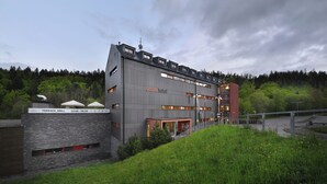 A modern hotel with a terrace, grill, and a view of a forested area. - Omnia Hotel Relax & Wellness (Janske Lazne)