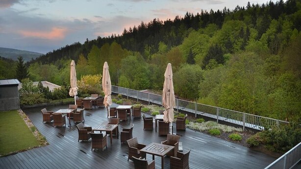 A covered outdoor seating area with tables and chairs, surrounded by a wooden deck and a railing. - Omnia Hotel Relax & Wellness (Janske Lazne)
