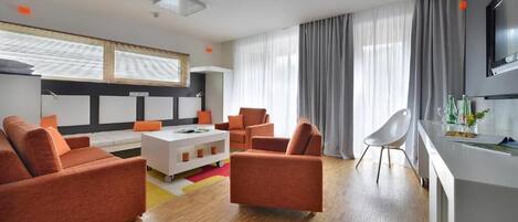 A modern living room with orange sofas, a white coffee table, and a kitchen area with a TV.